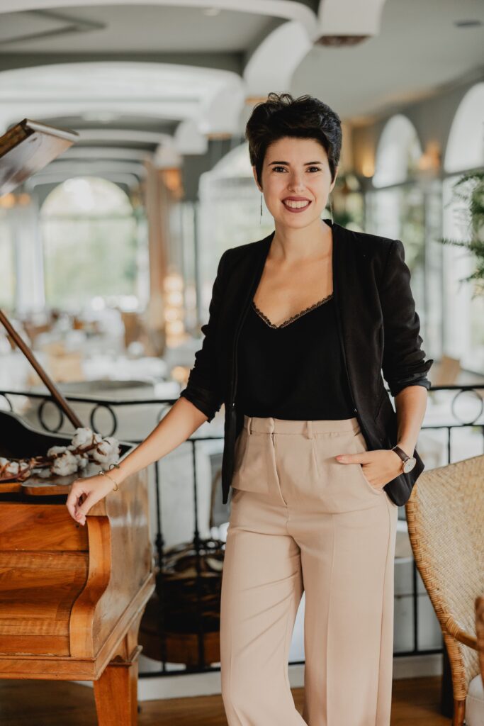Photo de Solène, la wedding planner qui couvre le Pays Basque et les Landes. Elle est debout à côté d'un piano dans un très beau lieu.