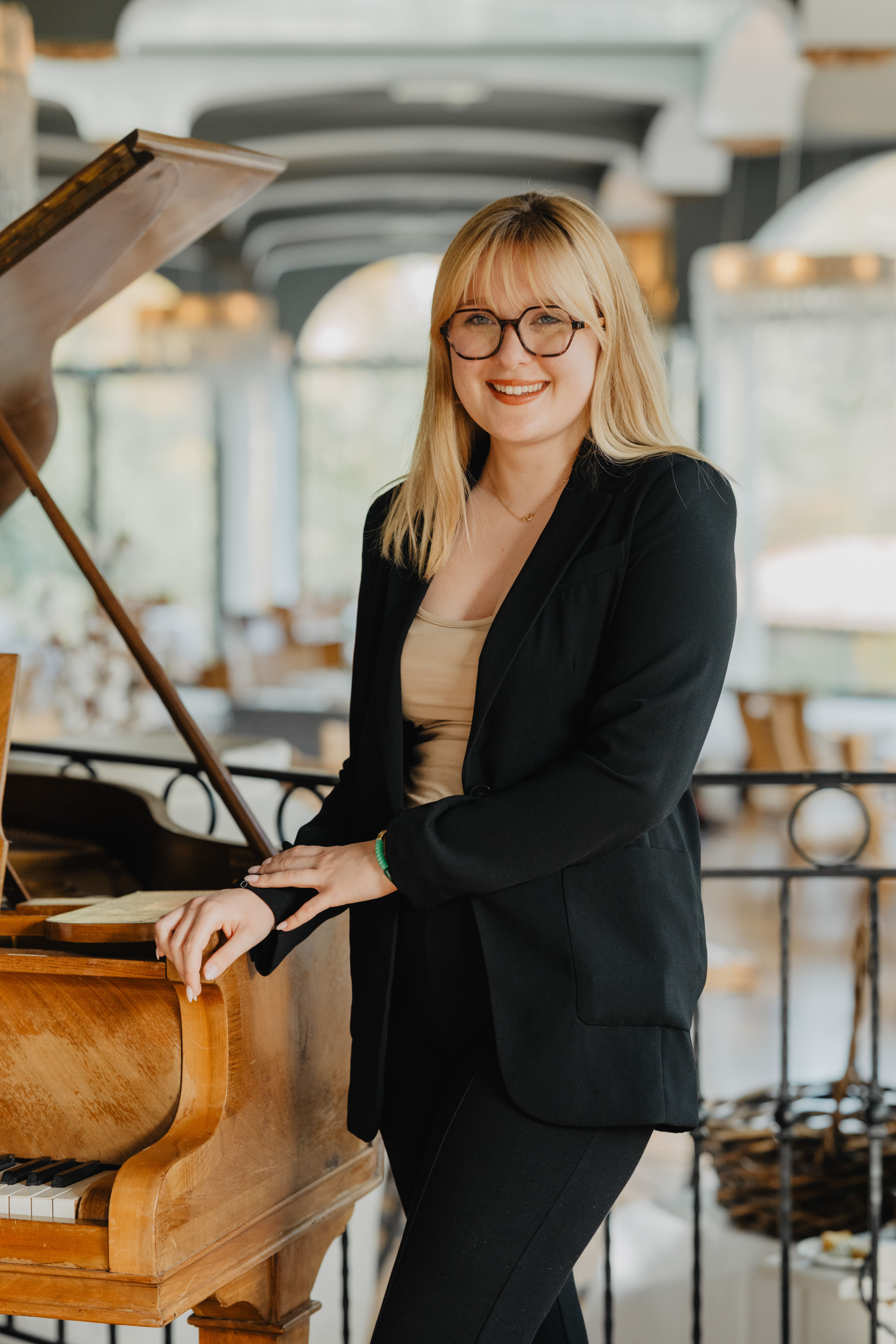 Photo de Mae, la wedding planner qui couvre l'Alsace. Elle est debout à côté d'un piano dans un très beau lieu.