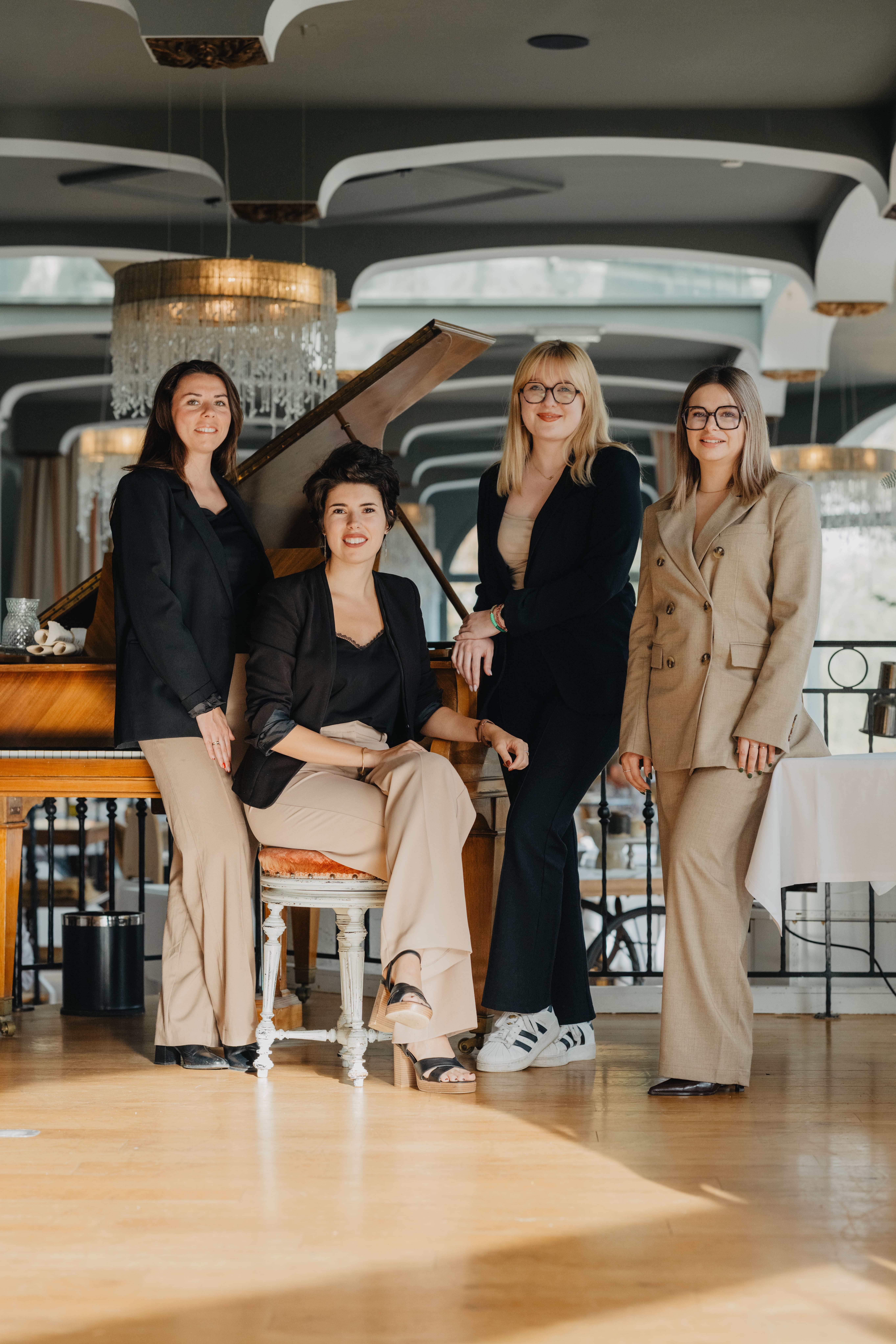 Photo des 4 wedding Planner de la franchise. Elles se tiennent debout à côté d'un piano, sauf Solène qui est assise