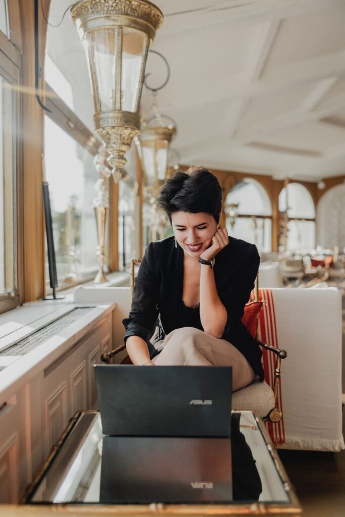 On voit Solène assise sur un sofa dans un cadre élégant en train de travailler sur son ordinateur